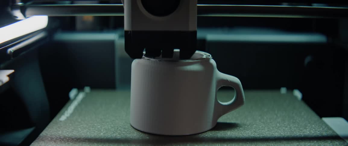 A 3d printer in operation creating a white ceramic mug in layers