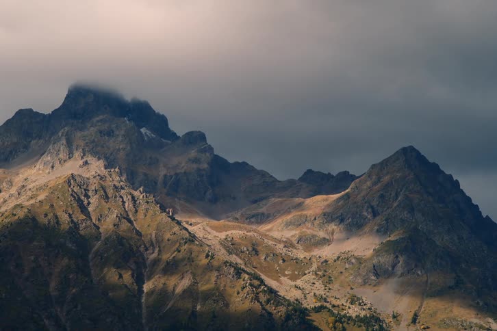 Sunlight shines on a mountain slope as clouds hang low over the peaks