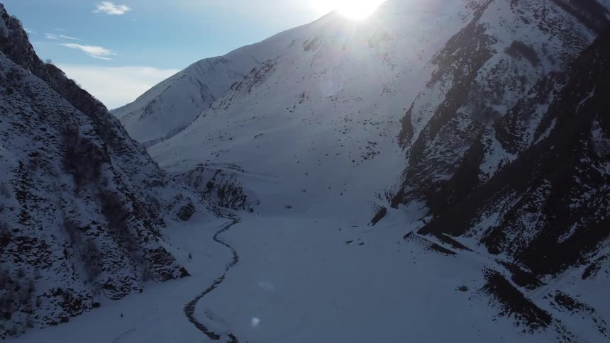 A winding path snaking through a snowcovered valley framed by towering snow capped mountains and a brilliant sun shining in the sky