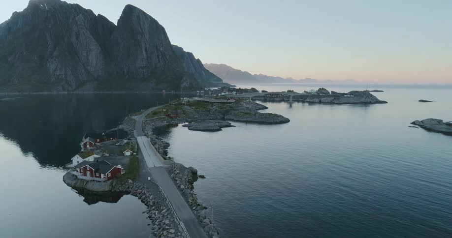 Highway on a narrow strip of land in the ocean passes buildings on route to a mountain