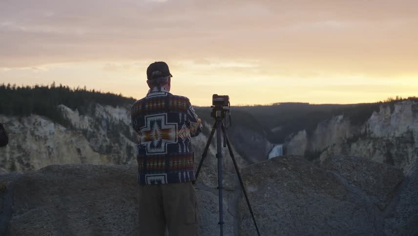 Man standing in front of a tripod with a professional camera in a mountain valley
