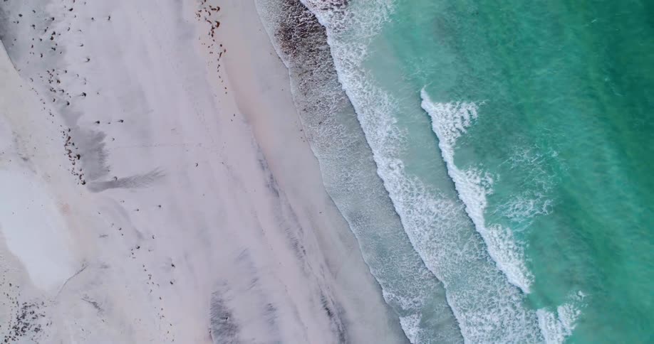 Birds eye view of waves crashing onto white sandy beach in the tropics