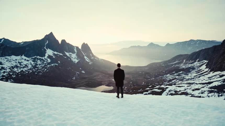 A person stands alone on a snow covered slope gazing out at a vast mountain range and valley