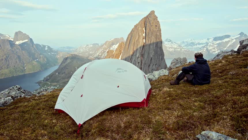 A man sits by his tent on the mountain