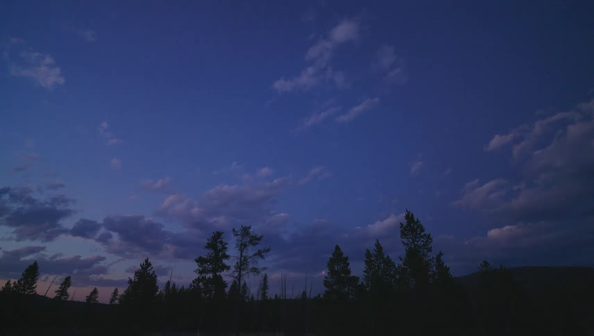 A pathway leads through a forested area under a twilight sky filled with scattered clouds