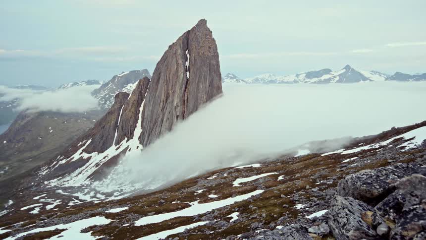 Low lying cloud floats past a rock formation on a slope in mountainous terrain on a winter day