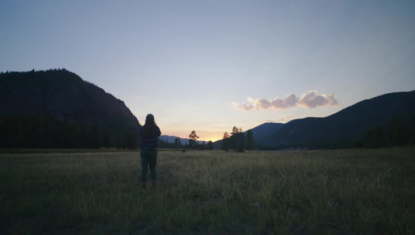 A woman stops in a field to straighten her hair then keeps walking