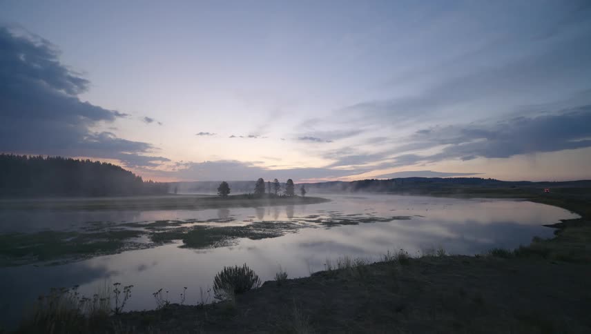 Landscape of a lake surrounded by mountains and vegetation and a dawn sky