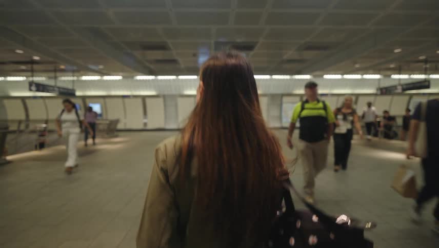 A woman with long hair is walking through a busy modern subway station