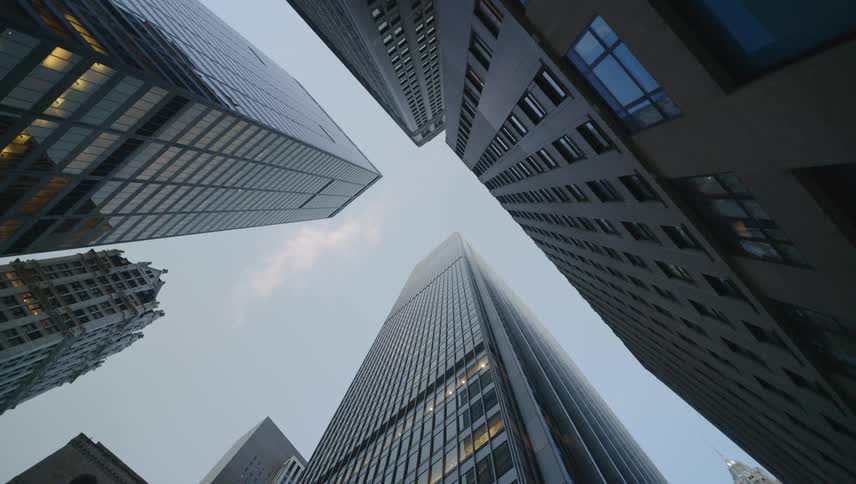 Tall buildings stretch upwards towards the sky as a person walks by below