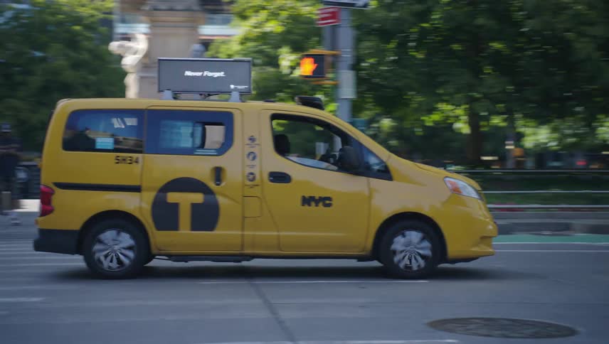 A yellow new york city taxi cab drives through a busy street