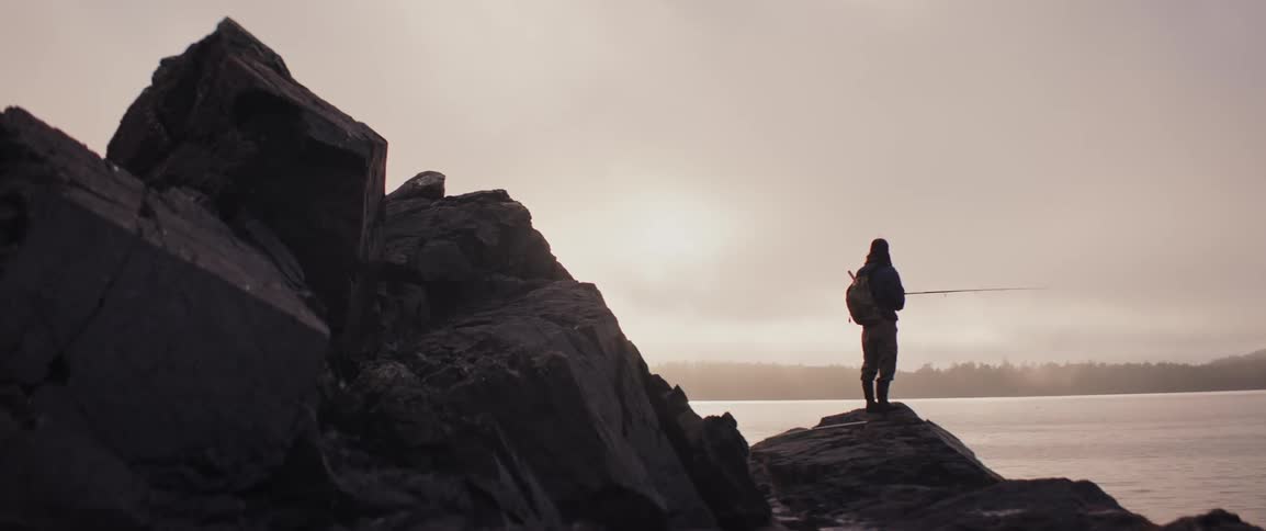 A silhouette of a person fishing on the sea shore on top of rocks as the sun sets