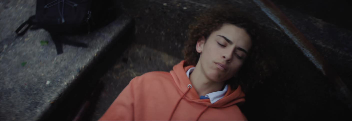 A young man in an orange coat is lying on the floor while talking