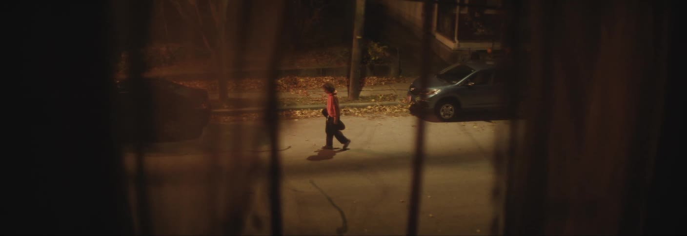 A view from inside a window of a person walking on the street next to parked cars