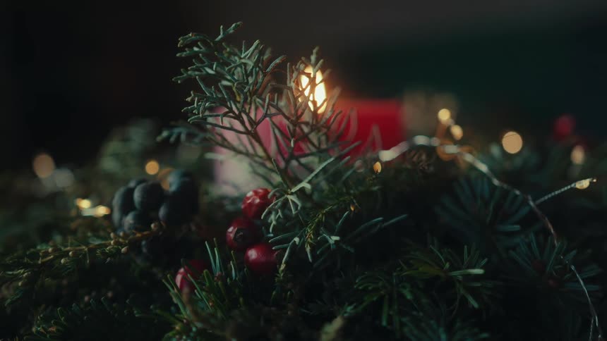 Christmas arrangement composed of green pine branches small red and blue fruits illuminated by the soft flame of a red candle in the background