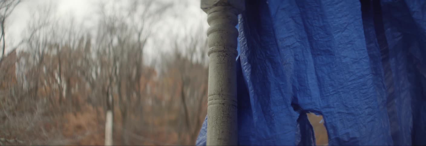 A white pickup truck is parked on a dirt path seen from a weathered wooden railing with a blue tarp draped over
