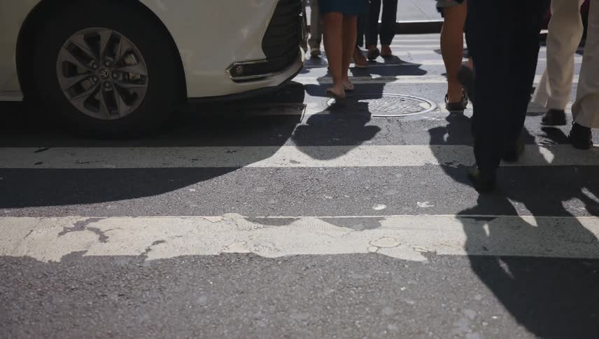 Pedestrians cross the road at a crosswalk mostly blocked by vehicular traffic during the daytime
