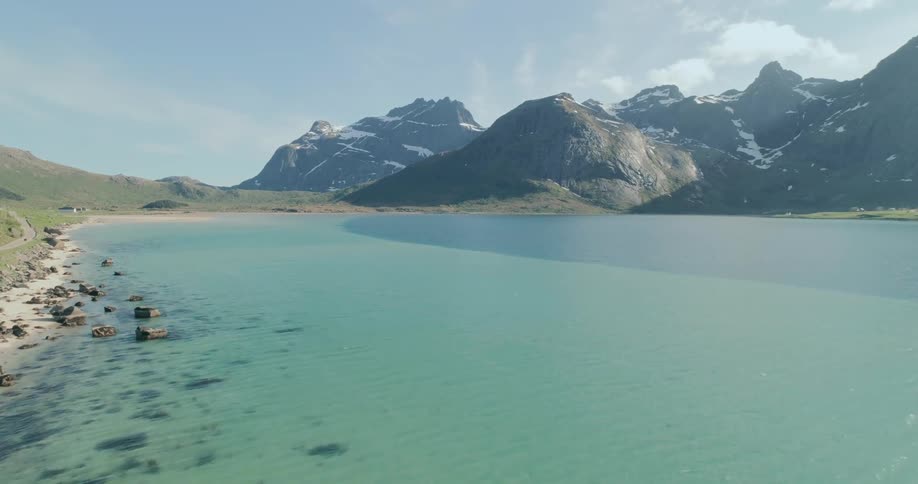 A clear turquoise body of water with a rocky shoreline and snowcapped mountains under a blue sky