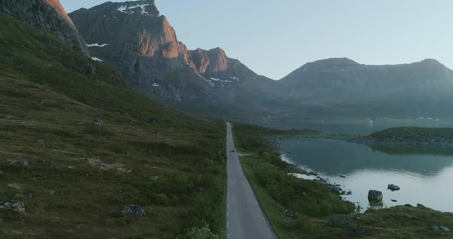 A winding road leads through a scenic landscape with mountains and a lake