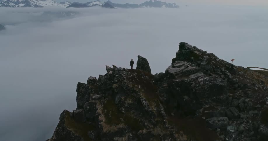 A person is standing on top of a mountain peak overlooking clouds