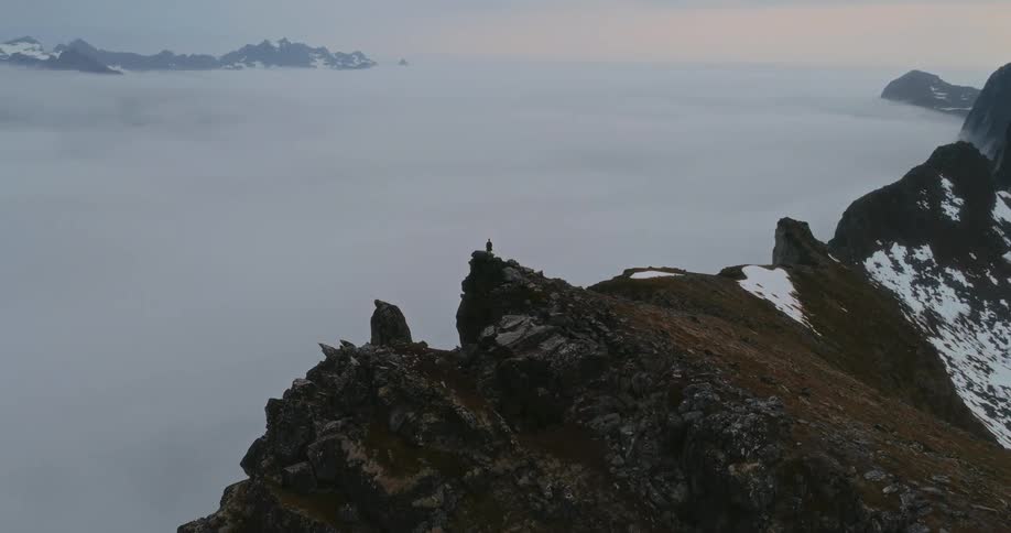 A hiker stands at the peak of the mountain above the clouds