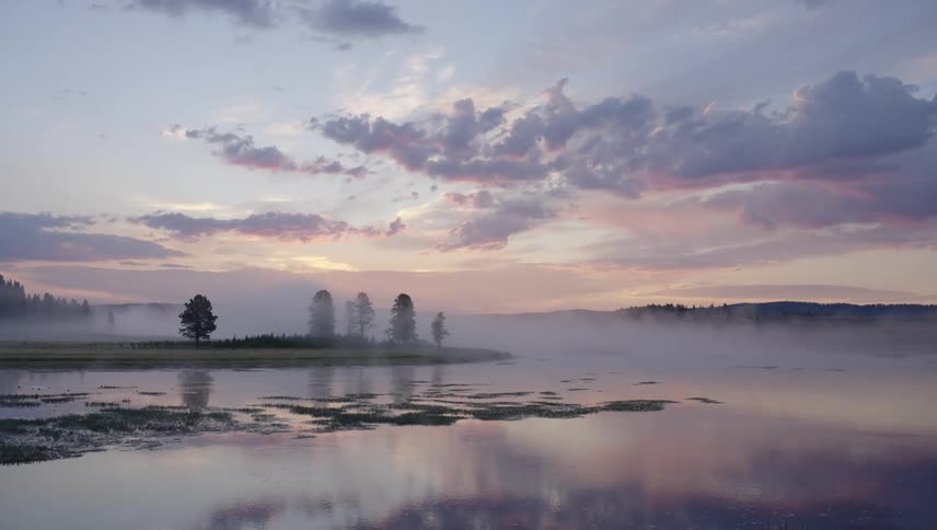 A landscape of a lake with still water reflecting the sky and there is a little fog hanging over the environment