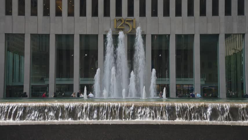 People walk past the large fountain in front of the building
