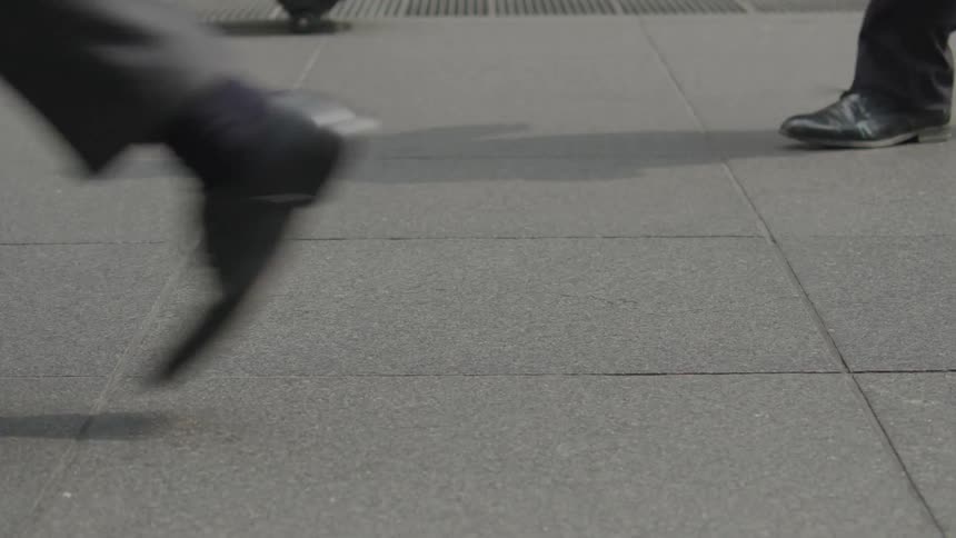 A closeup of a mans feet walking down a city sidewalk