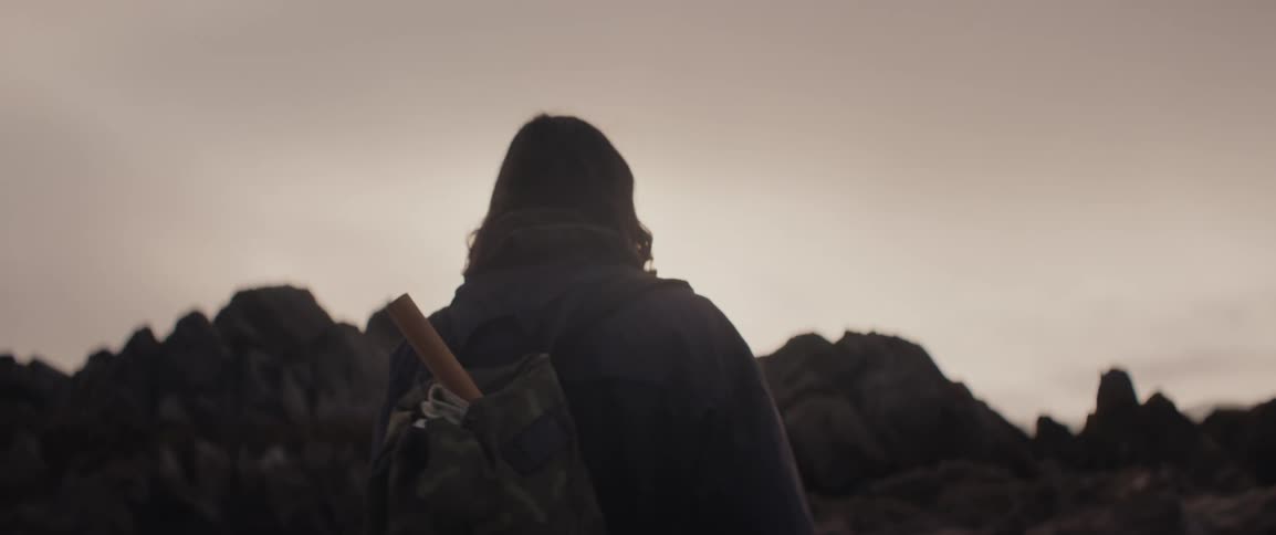 Man with fishing tools in his backpack walks towards a rocky outcrop on the beach
