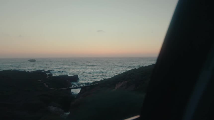 A car drives past the shore at sunrise