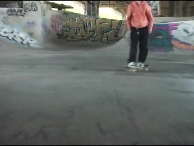 A child in a pink shirt is performing a skateboard trick inside a skatepark with graffiticovered walls and pillars