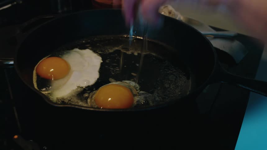 A man cracks eggs into the frying pan