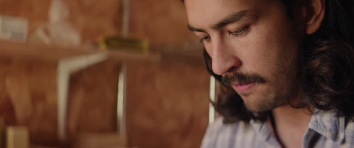 Closeup of a man with long hair and a mustache focused on his work in a workshop