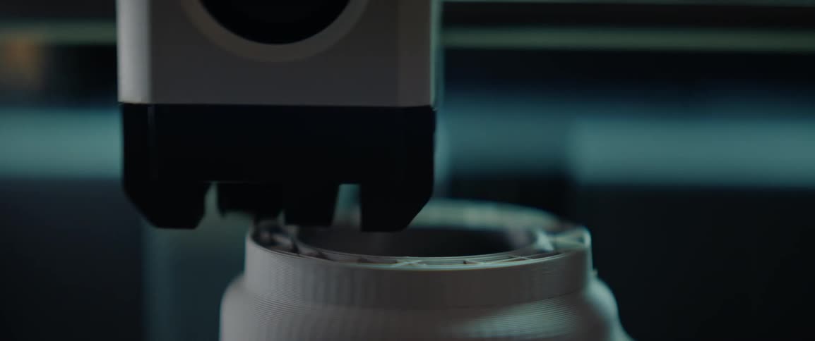 A closeup view of a 3d printer nozzle in the process of printing a cylindrical object with visible layers