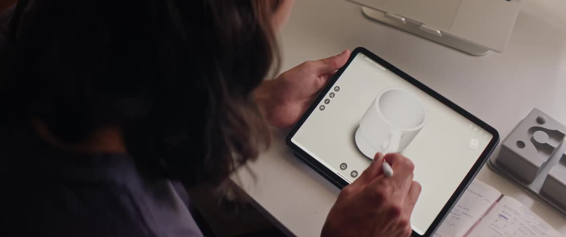A man using a stylus to draw a 3d model of a mug on a tablet