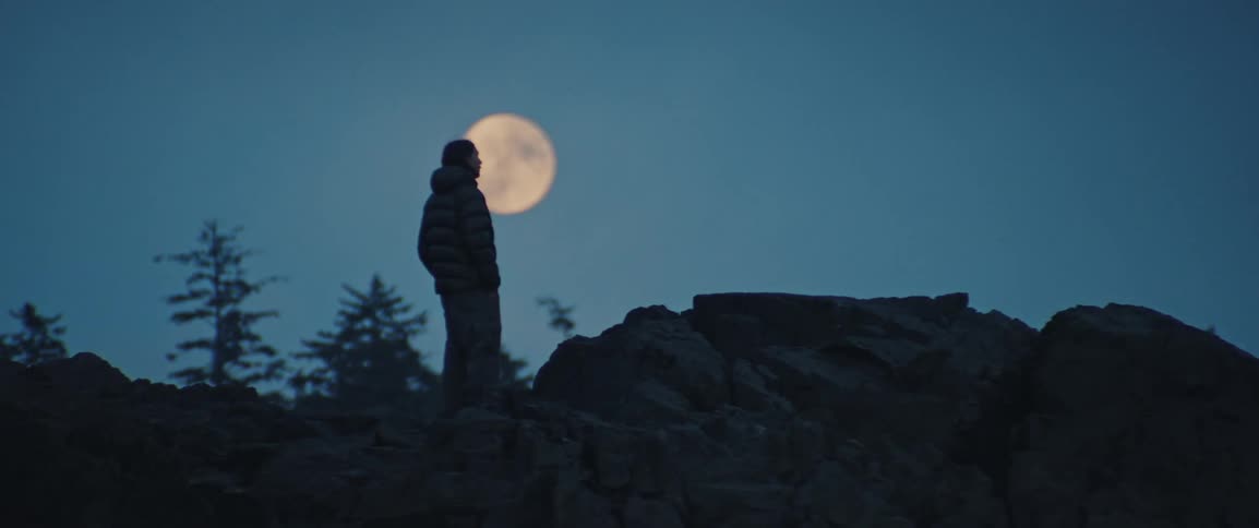 Silhouette of a man in a rocky area framed against the full moon