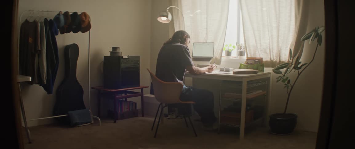 A longhaired man working at a desk in their home office during the day