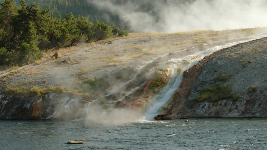 The stream gives off mist as it falls off the shore