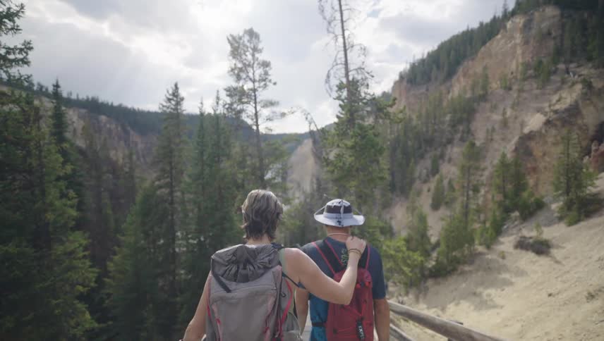 Couple with backpacks descending a wooden staircase in a mountain valley