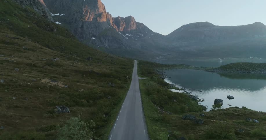 A solitary road winding through a rugged landscape with mountains and a fjord