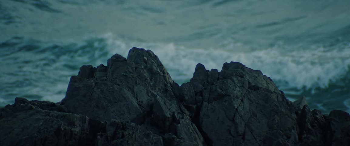 Strong ocean waves swell and break behind jagged rocks