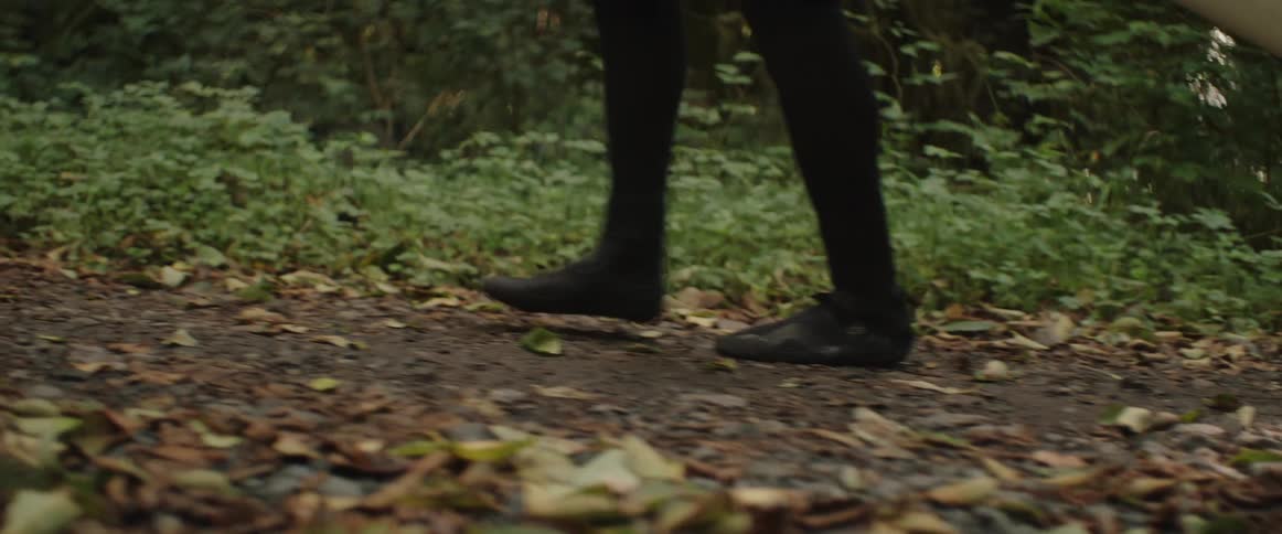 The feet of a person in a wetsuit walking along a forest path