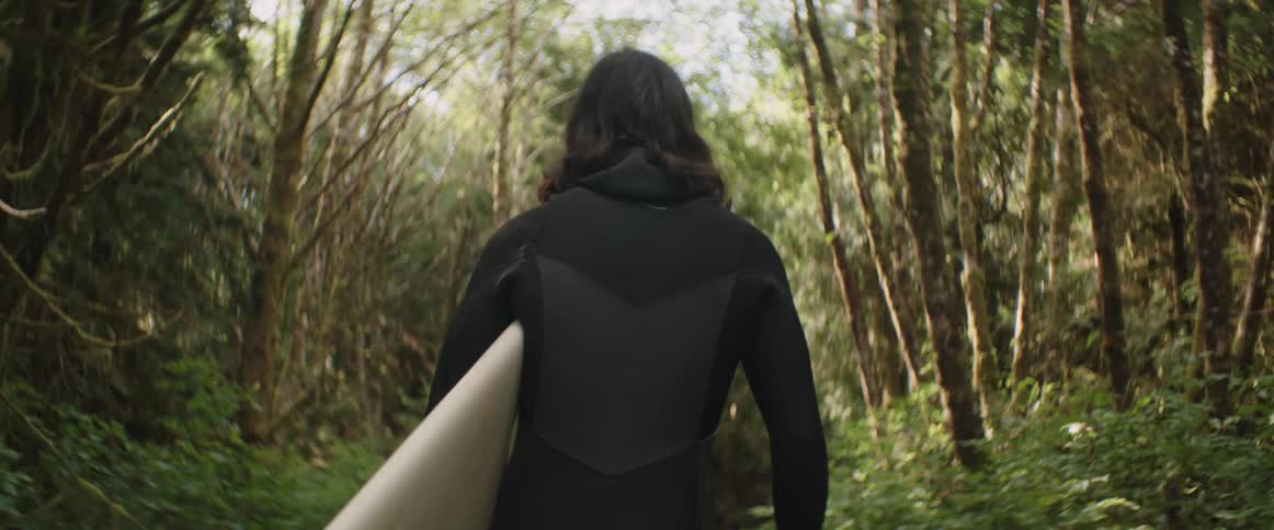 Person holding a surfboard walks through the tropical forest