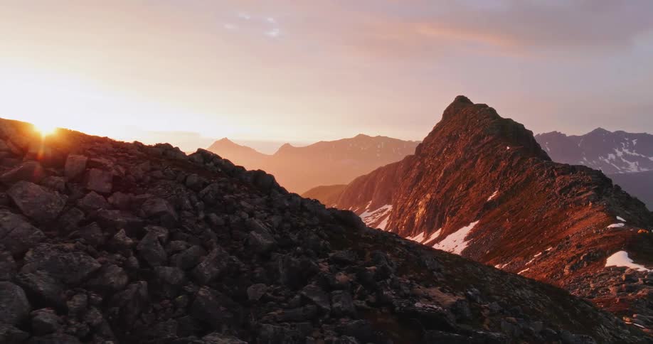 A dramatic mountain peak bathed in the warm glow of a setting sun with a range of mountains stretching into the distance