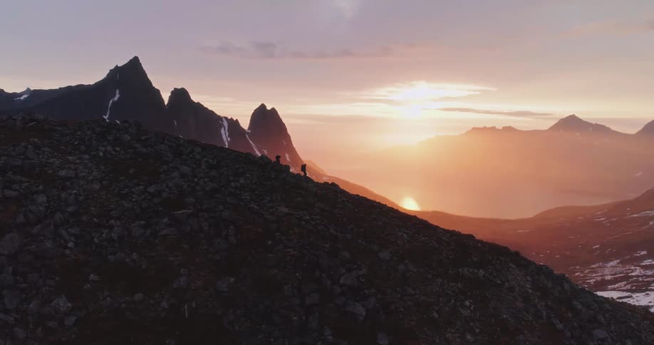 Silhouette of two people walking down a  mountain valley with the sunrise on the horizon