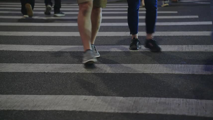 A group of pedestrians walking across a zebra crossing at night focusing on their legs and feet