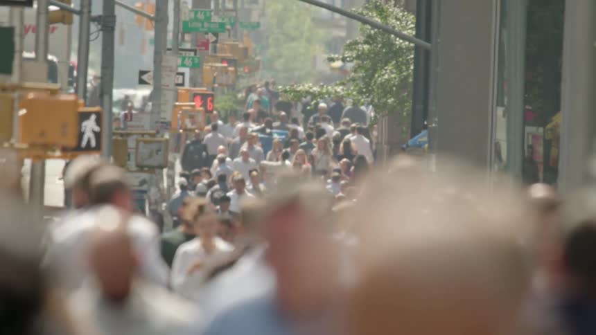 A large crowd of people walk down the sidewalk in a metropolis on a sunny summer day