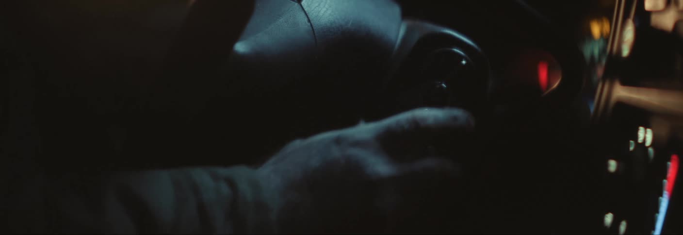 A hand is turning the key in a cars ignition at night with the dashboard lights illuminating