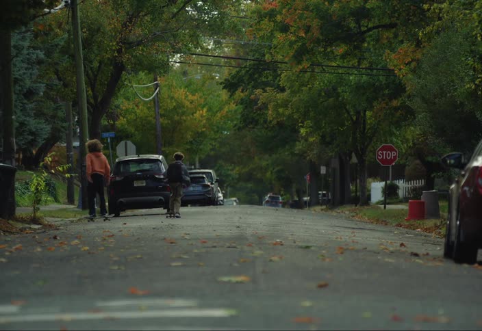 Two teenage boys are skateboarding down a residential street on an autumn day