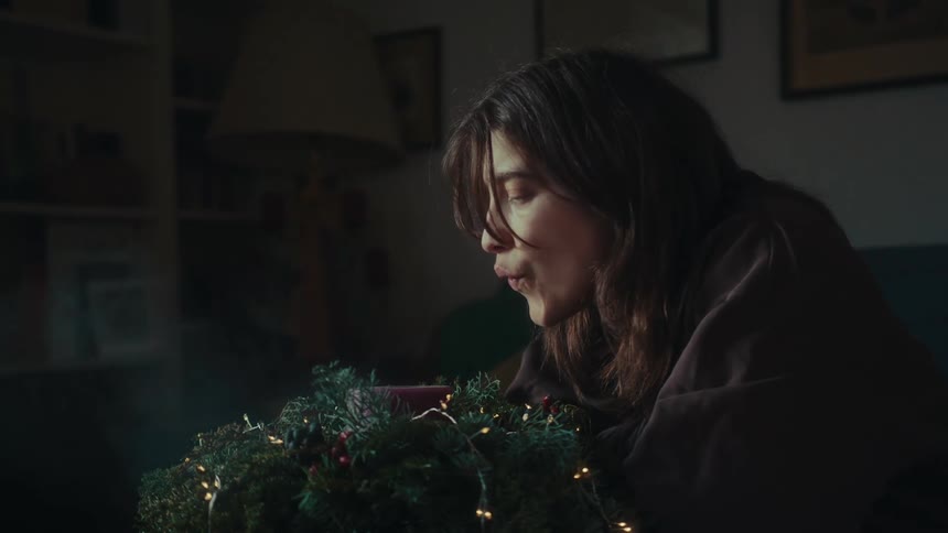 A lonely woman blows a christmas candle on a dimly lit living room